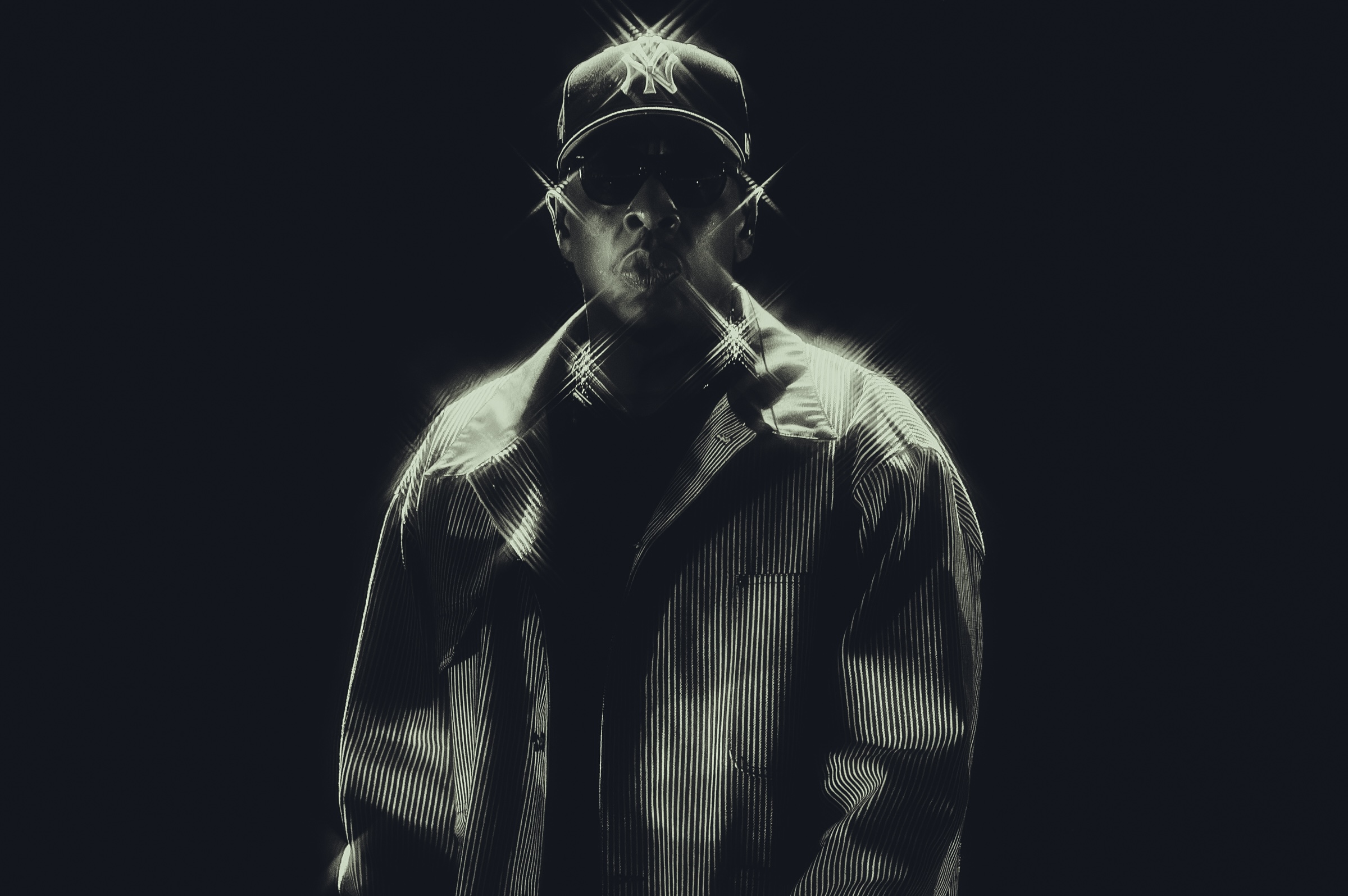 A person in a New York Yankees cap and jacket stands against a dark background, with light reflecting off them dramatically.