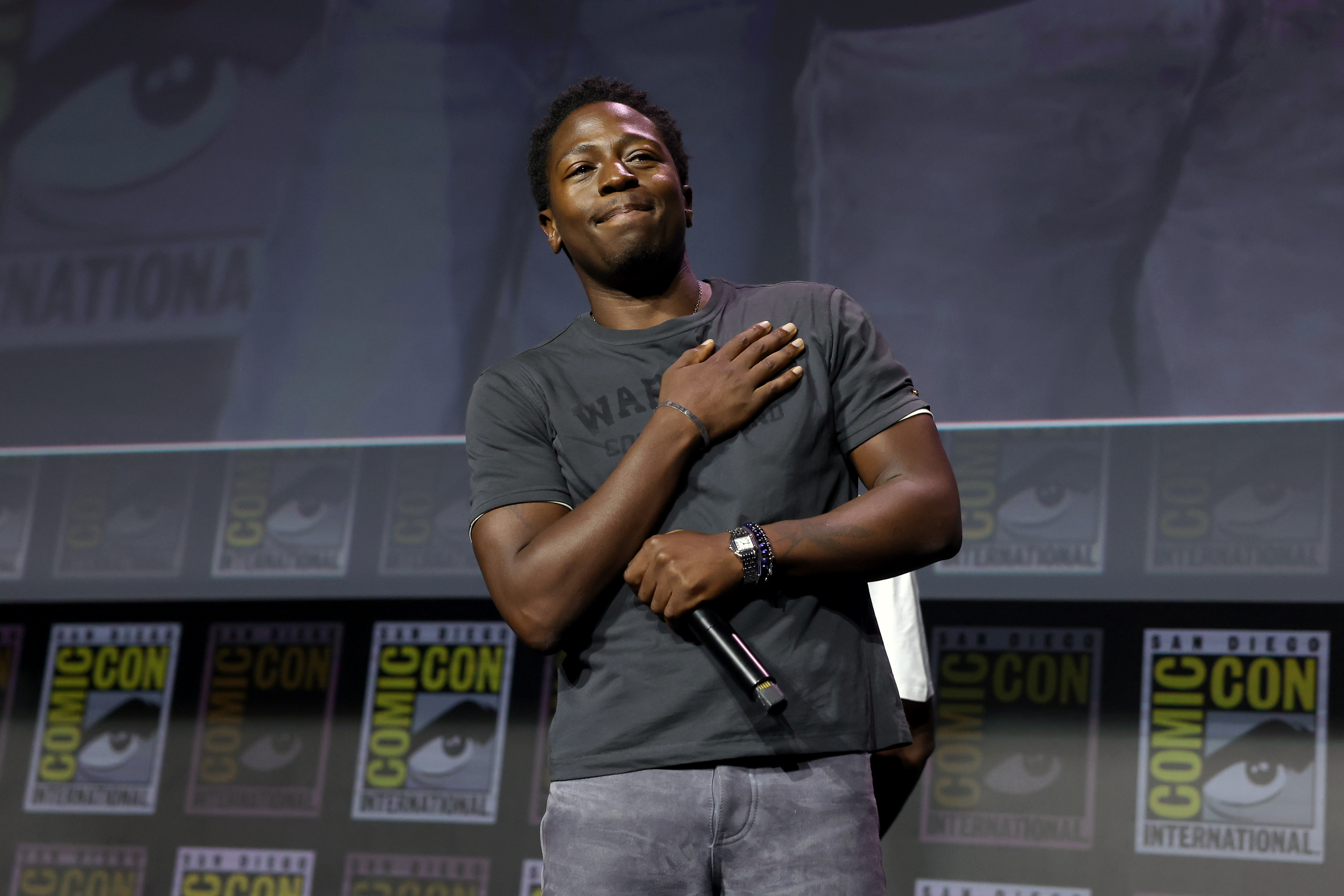 David Jonsson on stage at San Diego Comic-Con, holding a microphone, with Comic-Con logos in the background.
