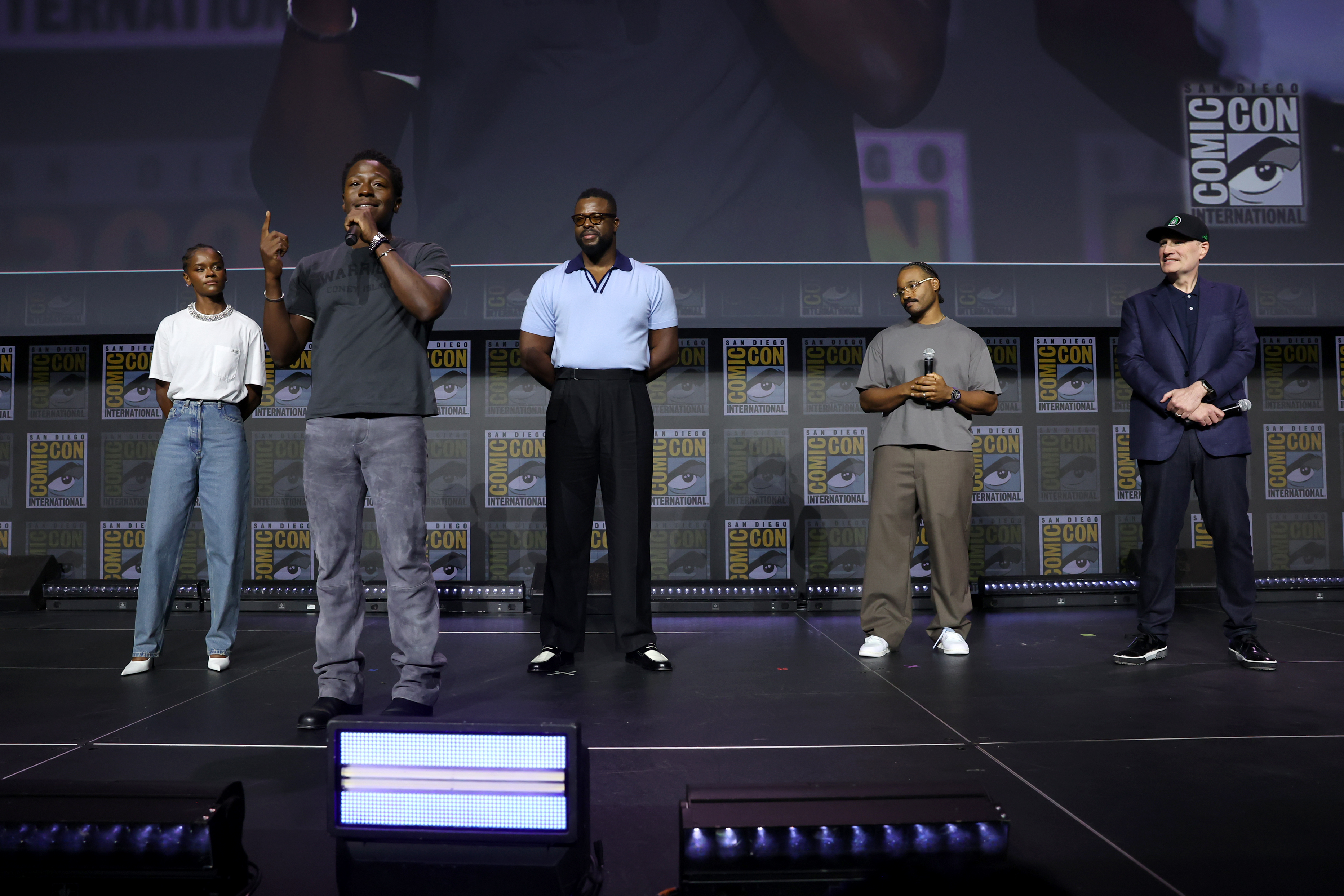 A group of five people on stage at Comic-Con, with one person speaking into a microphone.