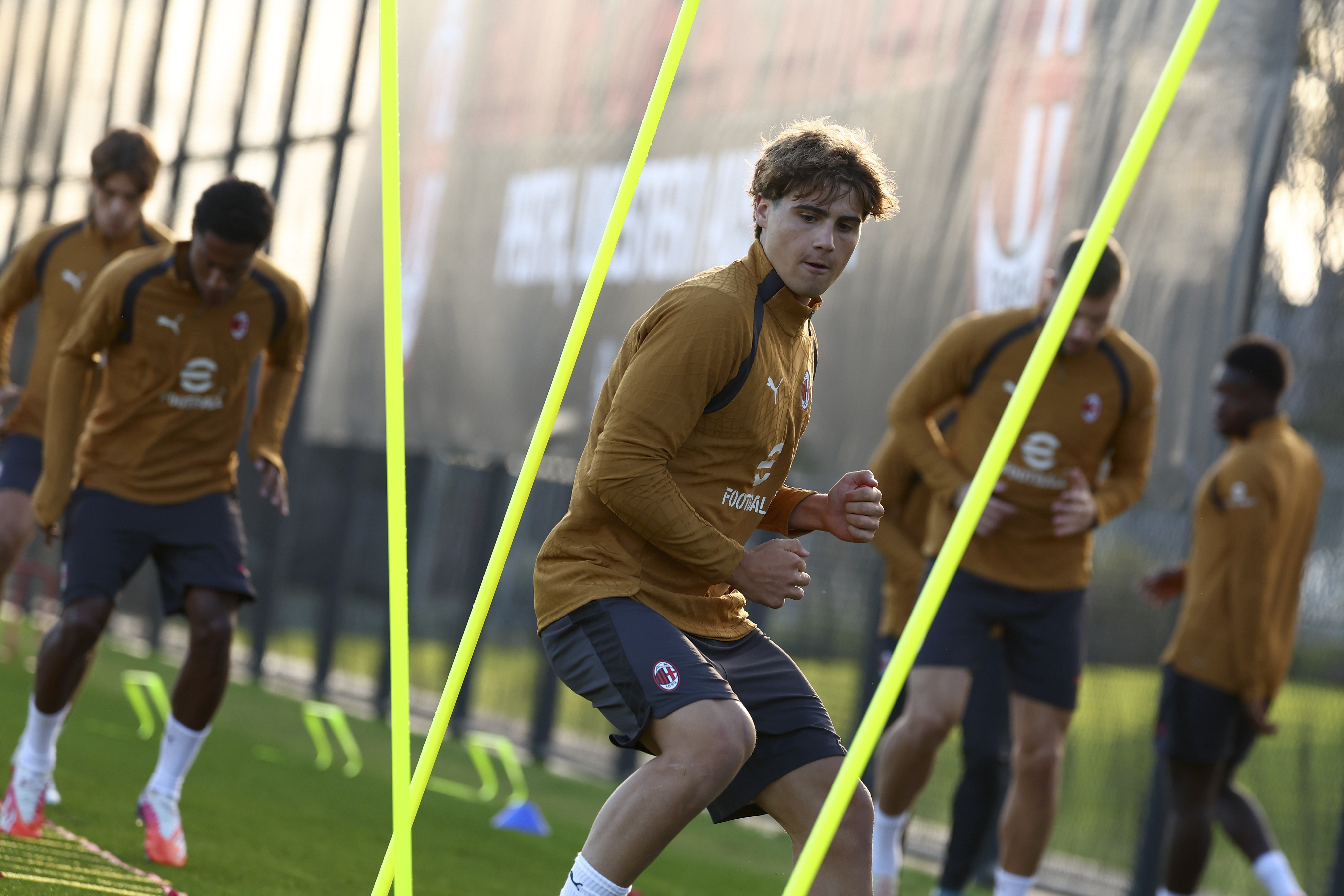 Soccer players in brown training kits practice agility drills on a field, with focus on one player in the foreground.