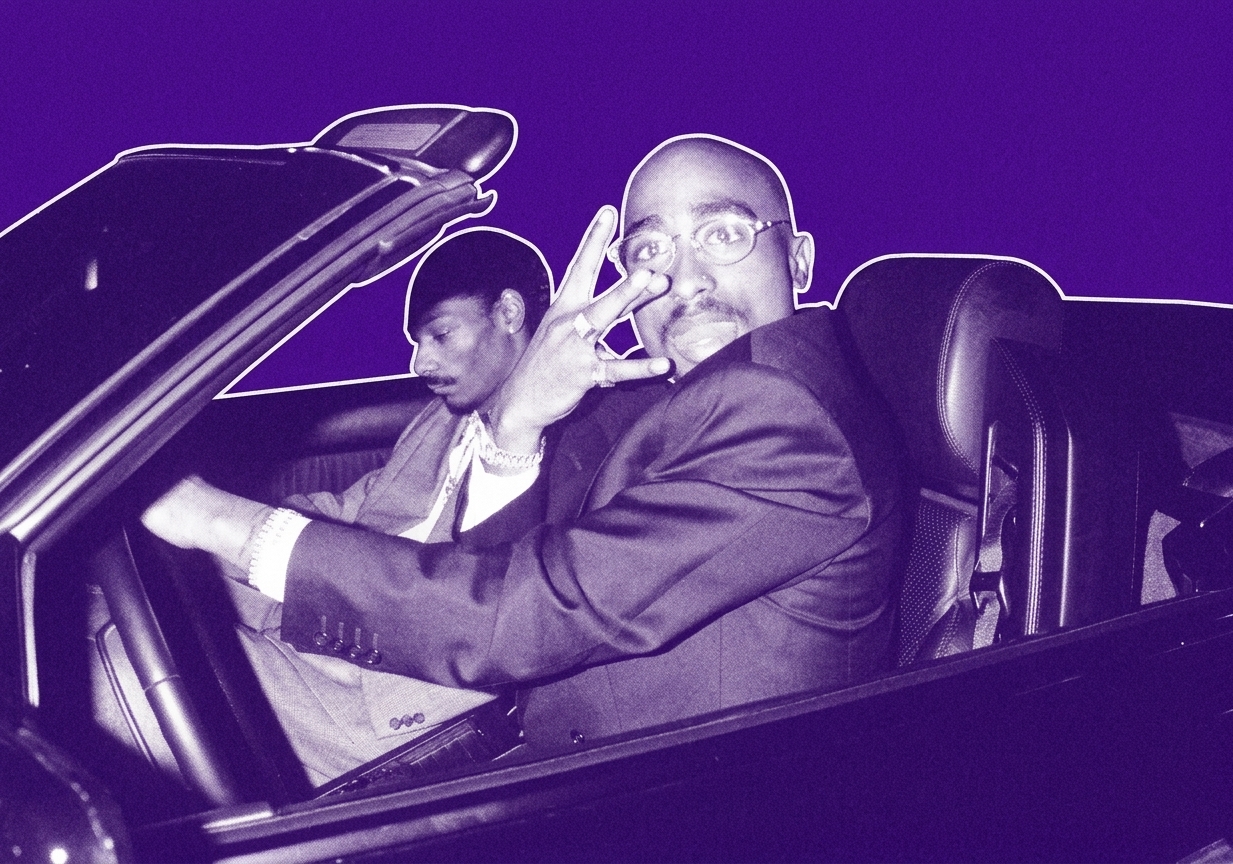 Tupac Shakur and Snoop Dogg in a convertible car, Tupac making a hand gesture, both dressed in suits.