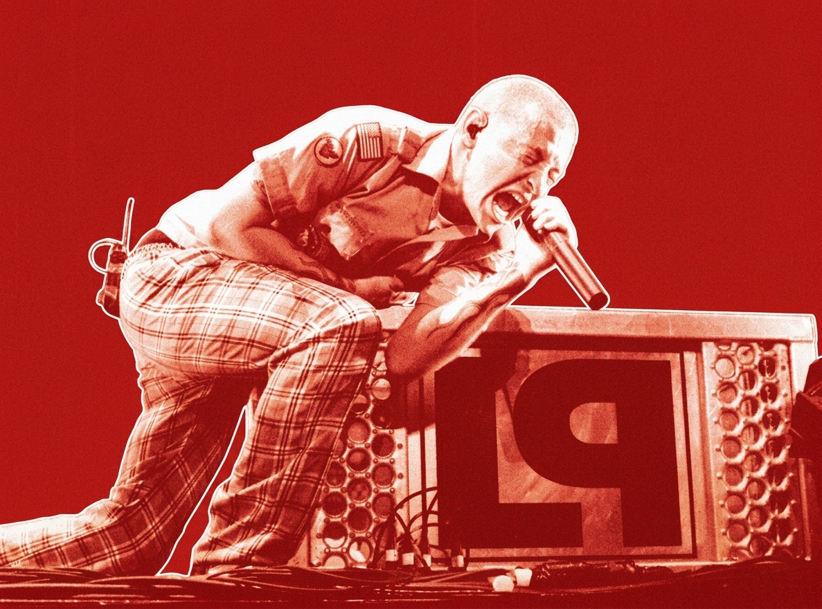 Chester Bennington of nu metal band Linkin Park passionately singing into a microphone, kneeling on stage with a red filter effect.