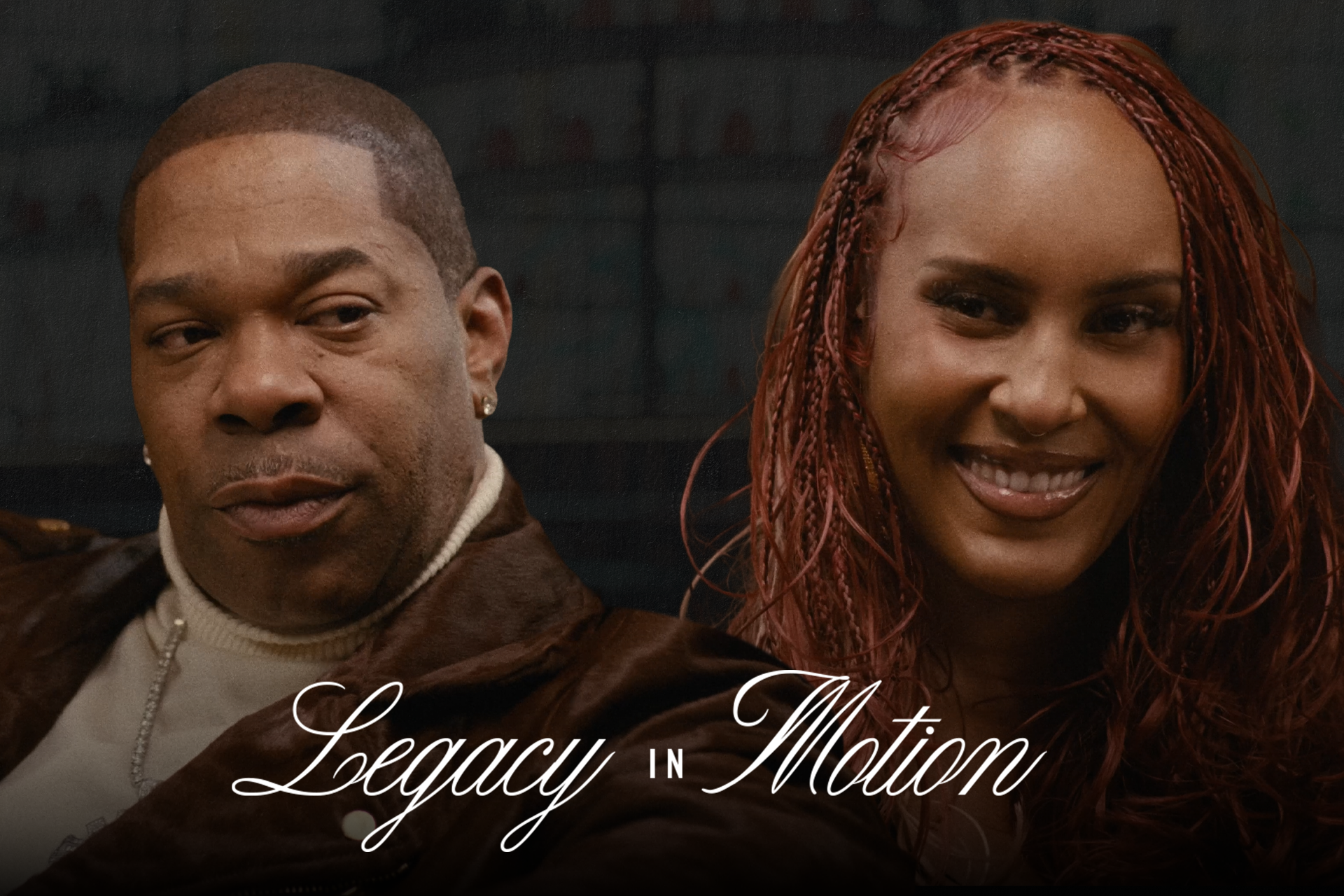 Two people seated, one with short hair and the other with long red braids, smiling. Text reads "Legacy in Motion."