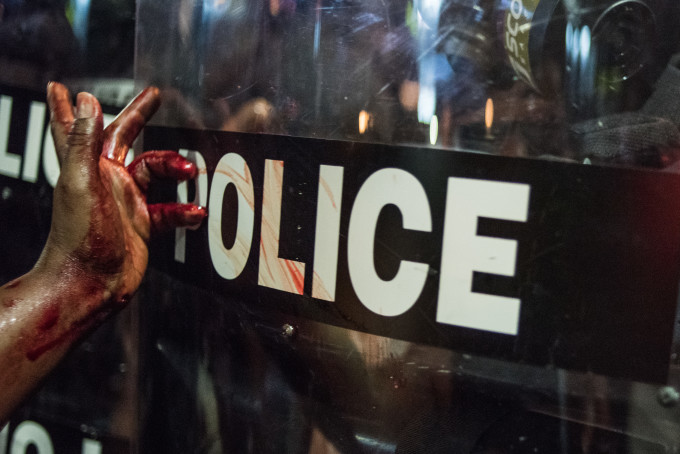 A wounded woman smears her blood on police riot shield.