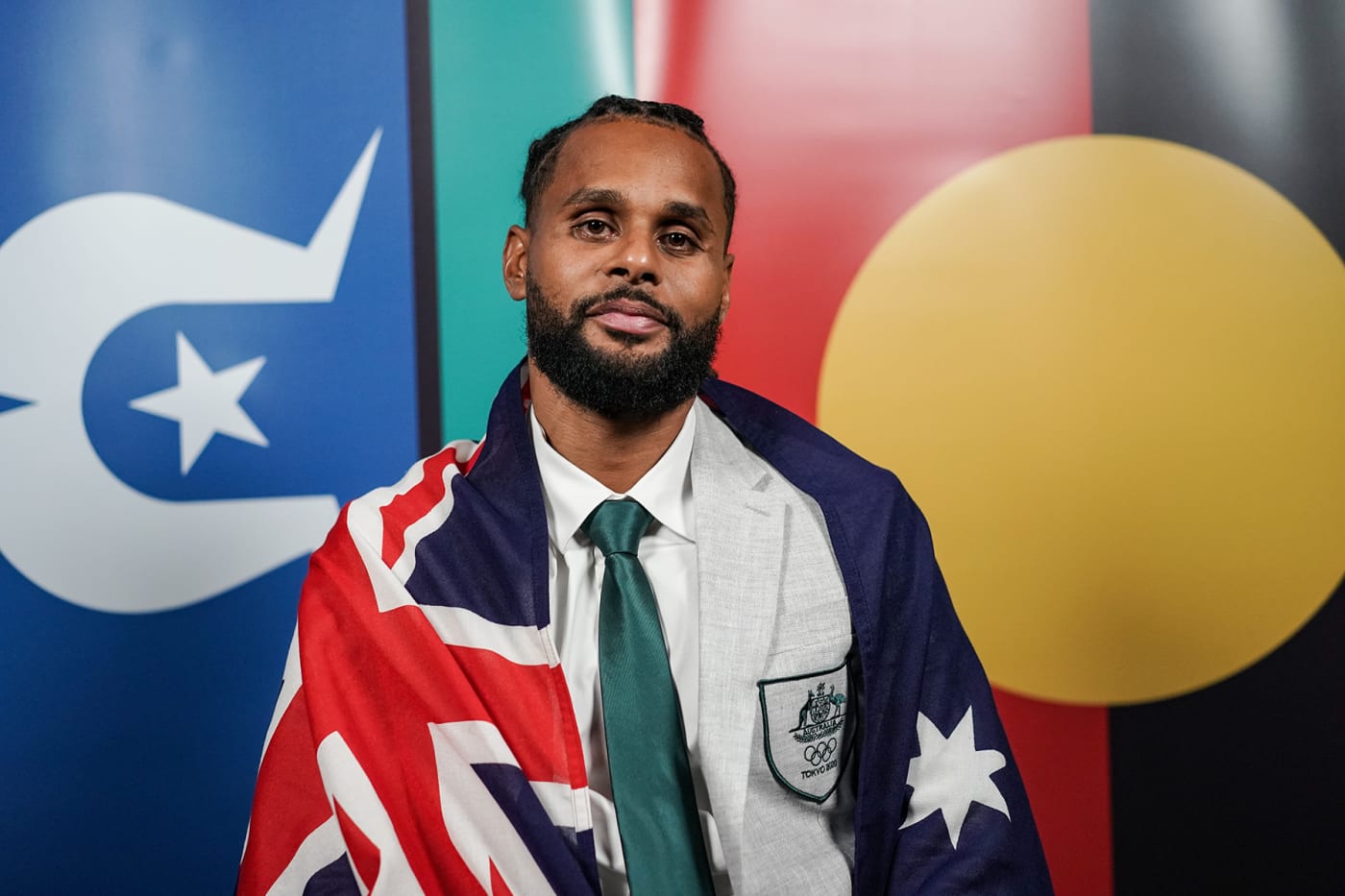Patty Mills posing with Australian, Torres Strait Islands and Australian Indigenous flags