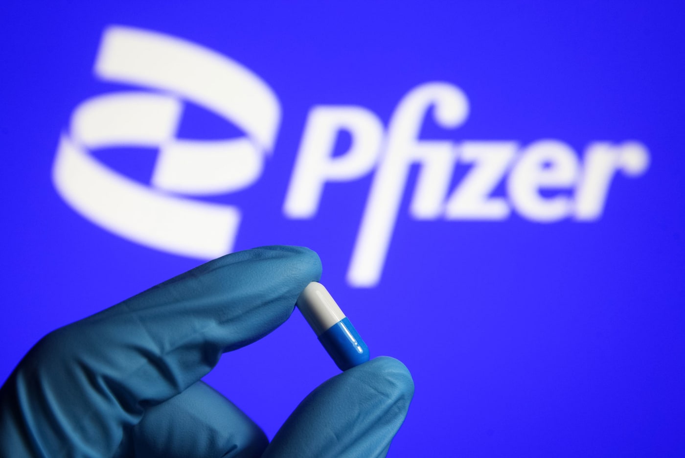In this photo illustration, a medicine pill is seen in a hand dressed in a medical glove with a Pfizer logo
