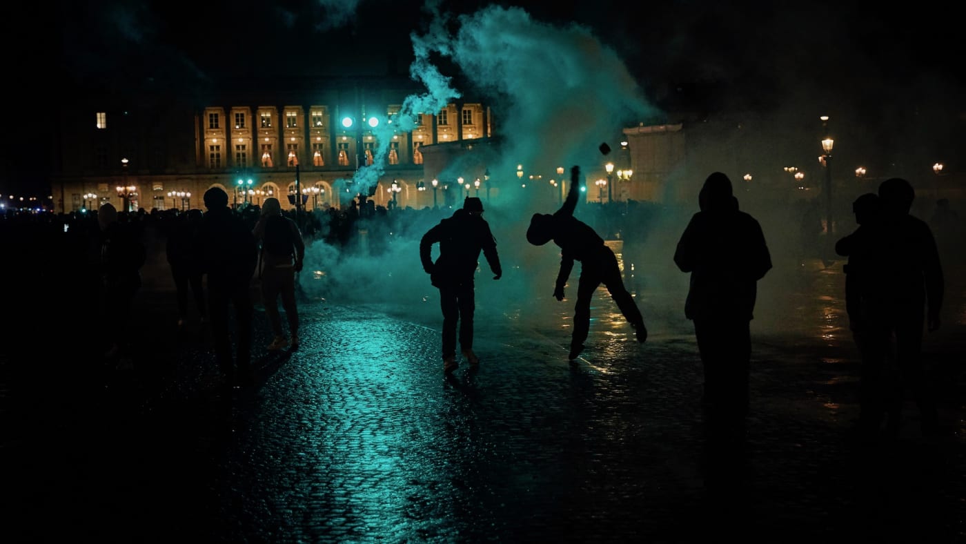 A protester throws a rock towards French Riot Police amidst clouds of tear gas during clashes