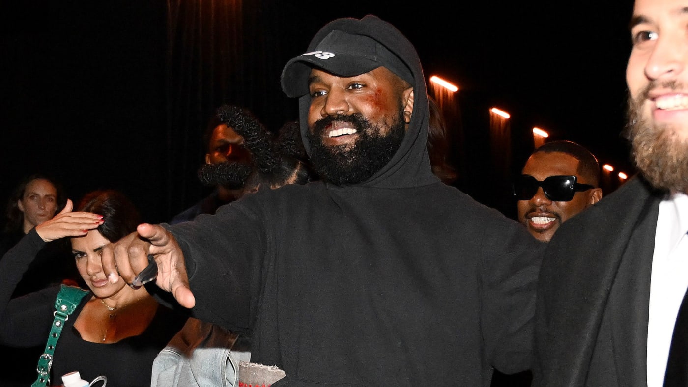 Ye is seen pointing and smiling at a fashion event