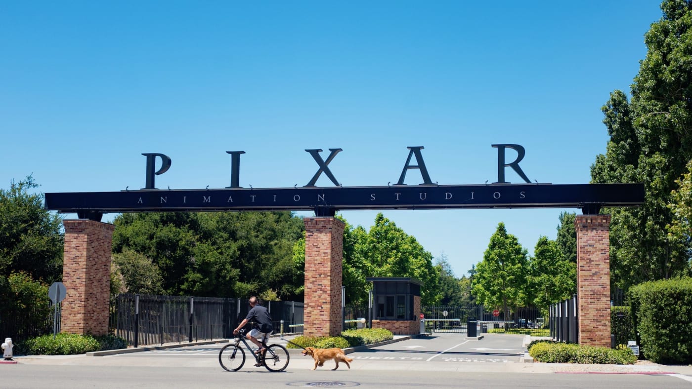 A man rides his bicycle and walks his dog past the entry gates at the headquarters of Pixar Animation Studios