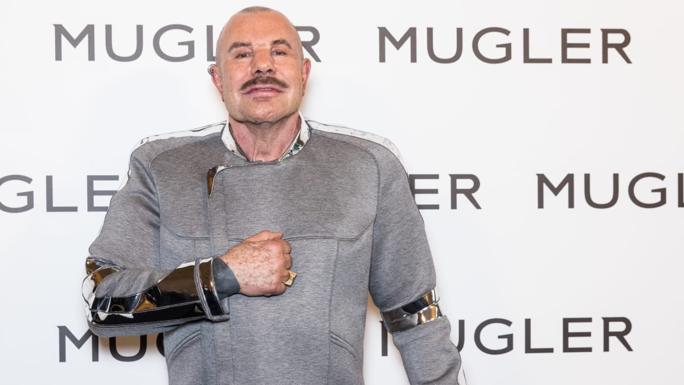 Manfred Thierry Mugler is pictured in front of a logo
