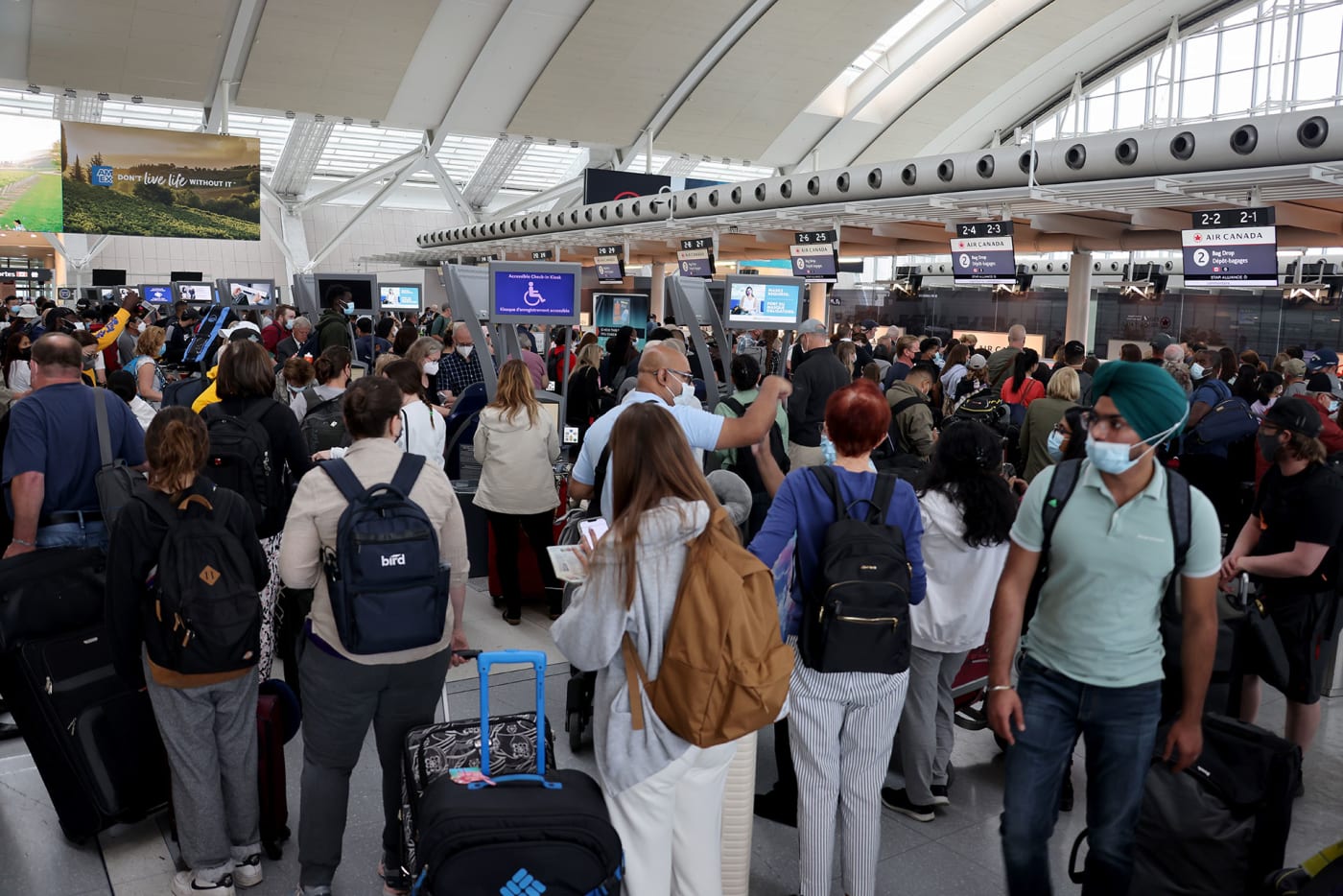 Travelers wearing face masks wait to check in at Toronto Pearson International Airport on June 30, 2022