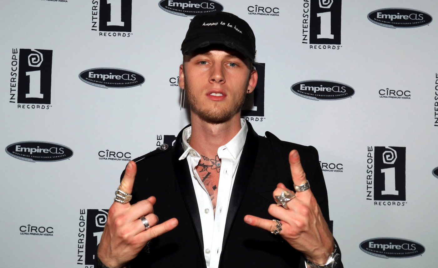 Machine Gun Kelly posing for a photow with devil horn signs.