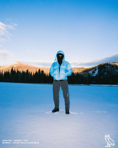 Model in a blue parka in the snow -  - OVO Drake